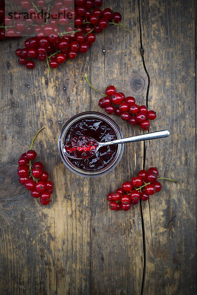 Marmeladenglas mit Johannisbeergelee und roten Johannisbeeren  Ribes rubrum  auf Holztisch  erhöhte Ansicht