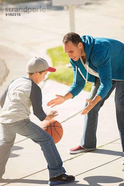 Vater und Sohn spielen Basketball in sonniger Einfahrt