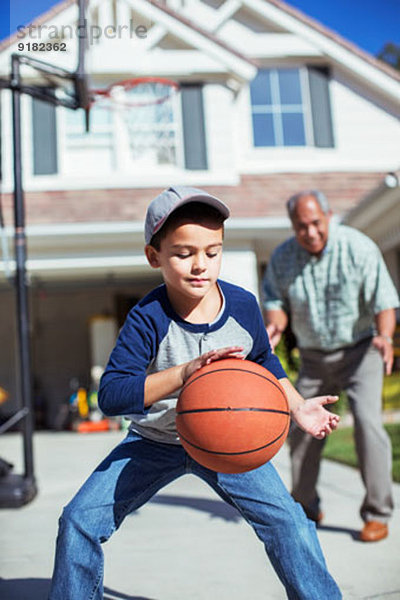Großvater und Enkel beim Basketballspielen in der Einfahrt