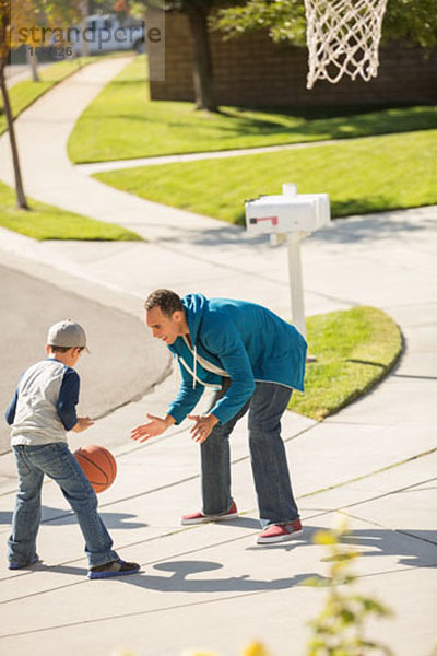 Vater und Sohn spielen Basketball in sonniger Einfahrt