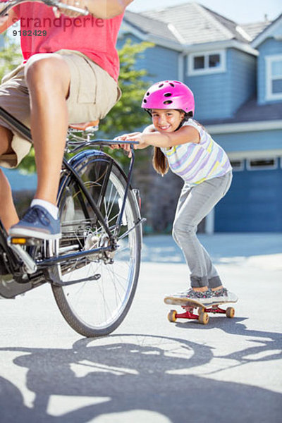 Tochter auf Skateboard schiebt Vater auf Fahrrad