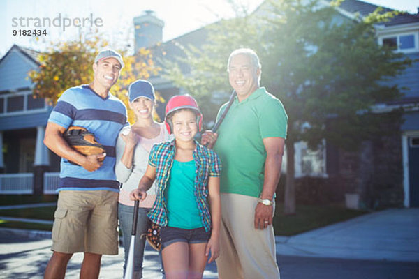 Porträt der lächelnden Mehrgenerationen-Familie mit Baseballschläger in der Straße