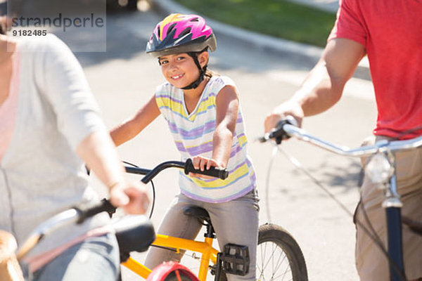 Porträt eines lächelnden Mädchens auf dem Fahrrad mit Eltern
