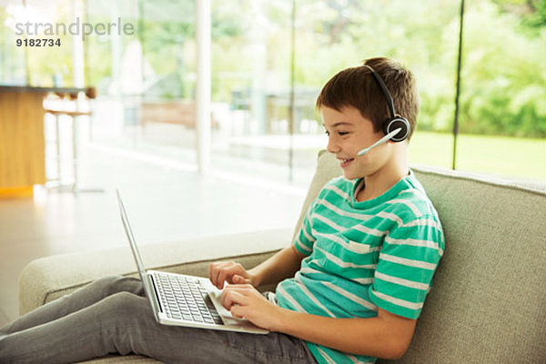 Junge mit Headset und Laptop auf dem Sofa