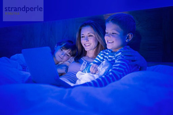 Mutter und Kinder mit digitalem Tablett im Bett