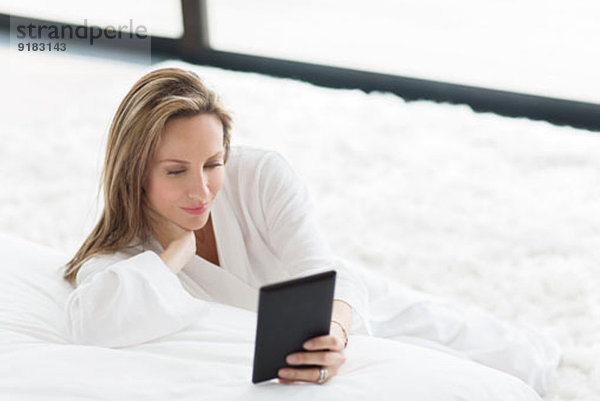 Frau im Bademantel mit digitalem Tablett im Schlafzimmer
