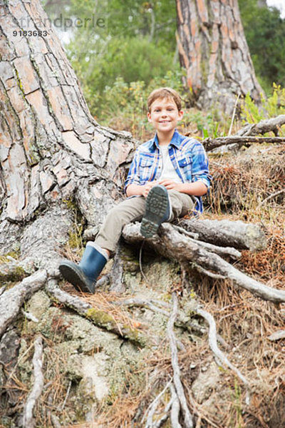 Junge auf Baumwurzeln im Wald sitzend