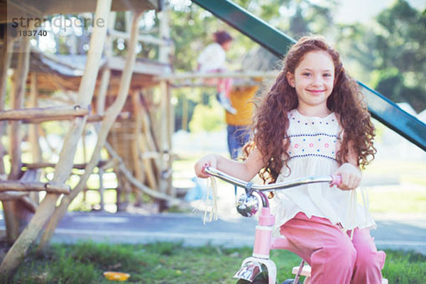 Lächelndes Mädchen sitzend auf dem Fahrrad auf dem Spielplatz