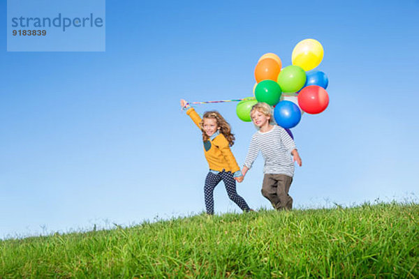 Kinder mit Luftballons auf grasbewachsenem Hügel