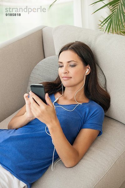 Junge Frau auf dem Sofa liegend Musik hören auf dem Smartphone