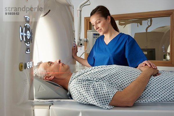 Röntgentechniker beruhigt den Mann  der in den CT-Scanner geht.