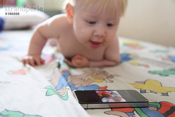 Baby spielt mit Smartphone im Bett