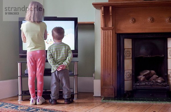 Rückansicht von Schwester und Bruder  die zu nah am Fernseher stehen und fernsehen.