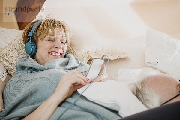 Reife Frau auf dem Bett liegend mit mp3-Player