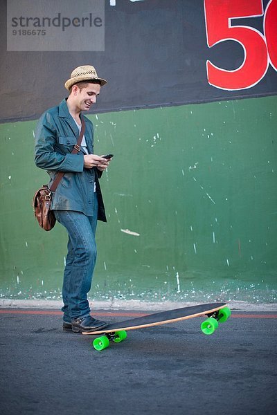 Mittlerer Erwachsener männlicher Skateboarder beim Lesen von Textnachrichten auf dem Smartphone