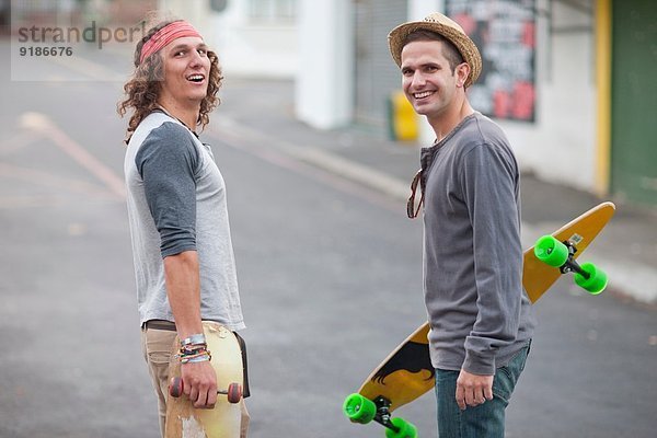 Portrait von zwei männlichen erwachsenen Freunden mit Skateboards auf der City Street