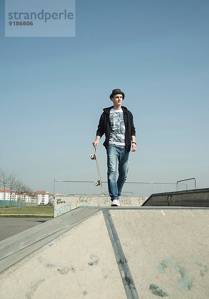 Junger Mann läuft durch den Skatepark und trägt Skateboard.