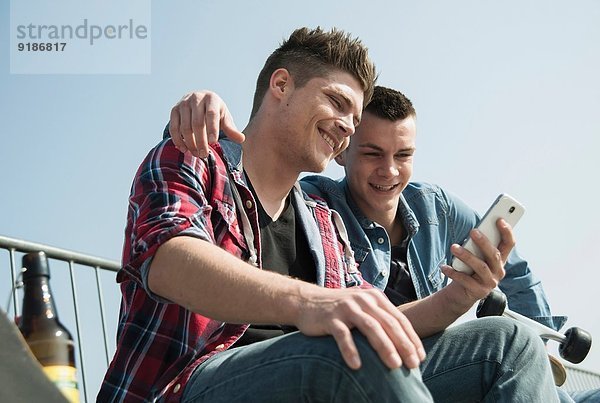 Junge Männer im Skatepark  mit Smartphone  Trinkflasche Bier