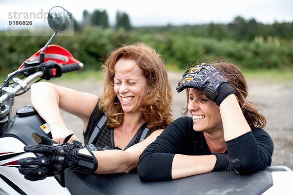 Zwei Motorradfahrerinnen  die sich auf das Motorrad stützen