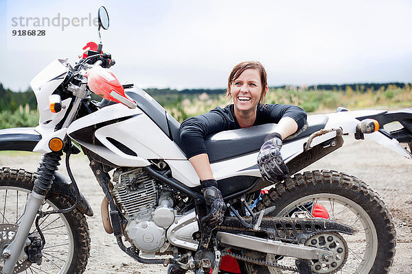 Porträt einer lächelnden jungen erwachsenen Motorradfahrerin mit Motorrad