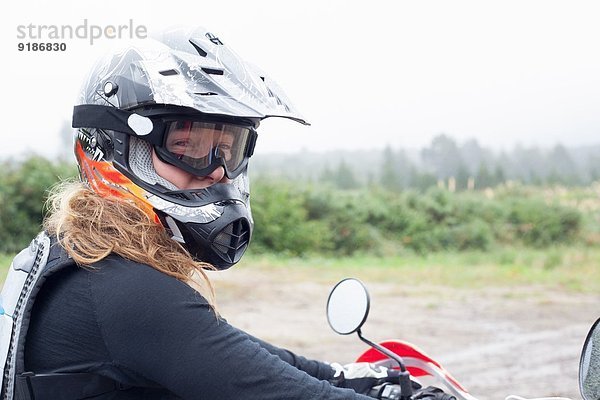 Porträt einer mittleren erwachsenen Motorradfahrerin mit Schutzhelm und Schutzbrille