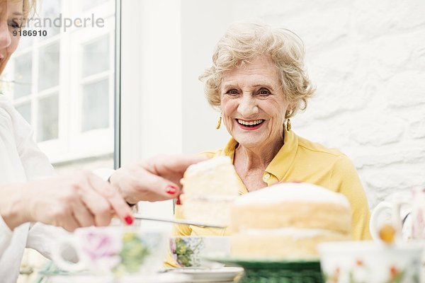 Seniorin und Tochter  Kuchen schneiden