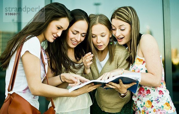 Vier junge Freundinnen schauen und lachen über das Notizbuch