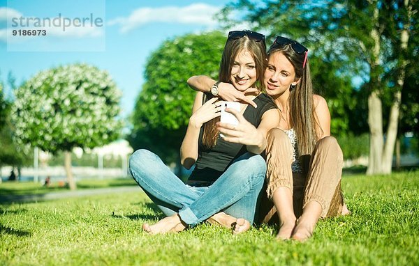 Zwei junge Freundinnen beim Selbstportrait auf dem Smartphone im Park