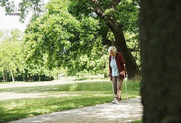 Ältere Frau  die durch den Park geht  mit einem Spazierstock.