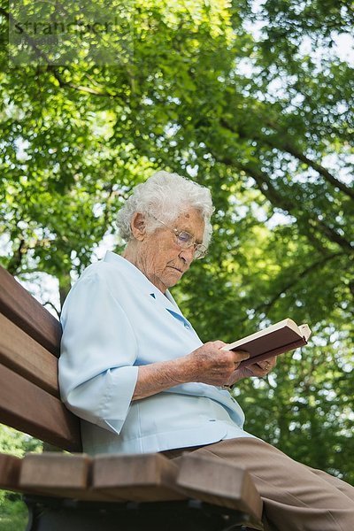 Seniorin sitzt auf der Parkbank und liest die Bibel.
