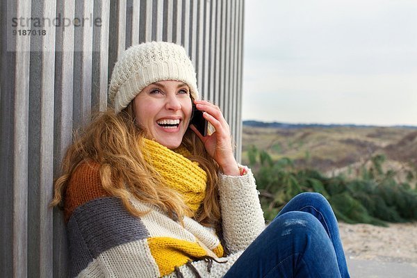 Porträt einer erwachsenen Frau  die auf einem Smartphone an der Küste chattet.
