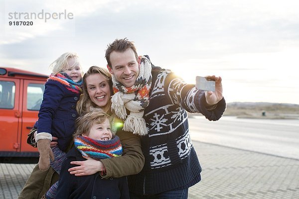 Mittlerer erwachsener Mann  der einen Familien-Selfie auf dem Küstenparkplatz nimmt