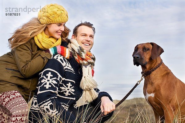 Lächelndes mittleres erwachsenes Paar und Hund an der Küste