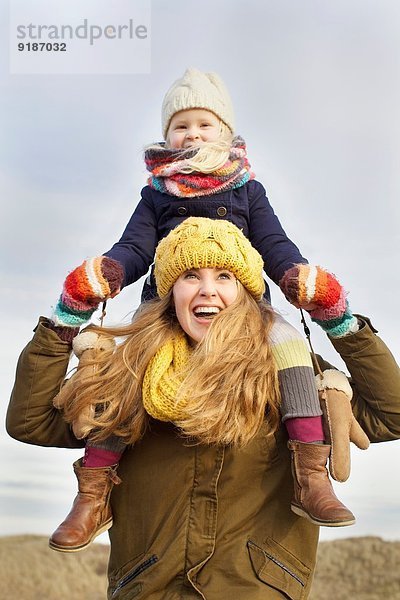 Lächelnde mittlere erwachsene Frau mit Tochter auf den Schultern an der Küste
