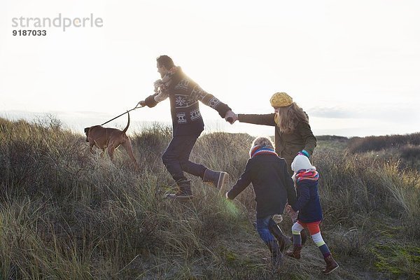Mittleres erwachsenes Paar  das mit seinem Sohn  seiner Tochter und seinem Hund in den Sanddünen spazieren geht.