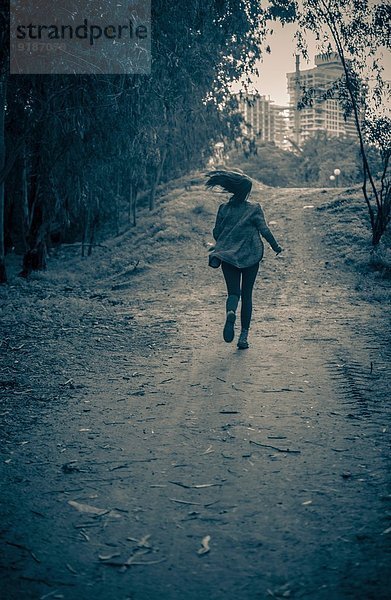 Junge Frau rennt von der Gefahr auf den Feldweg zu den Wohnblöcken