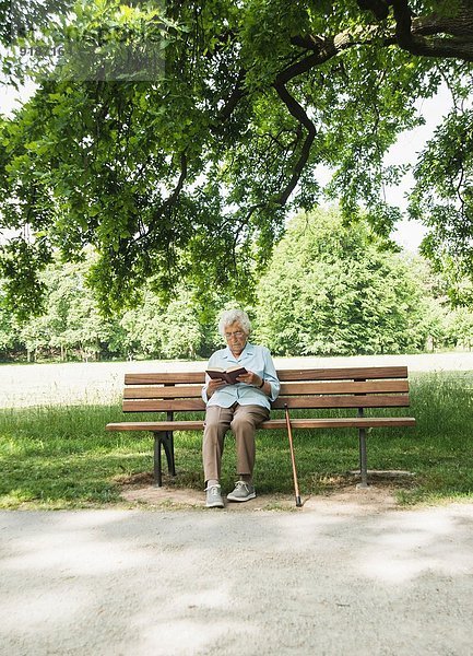 Seniorin sitzt auf der Parkbank und liest die Bibel.