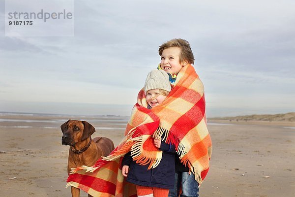 Porträt eines dreijährigen Mädchens und Bruders in Decke am Strand  Bloemendaal aan Zee  Niederlande