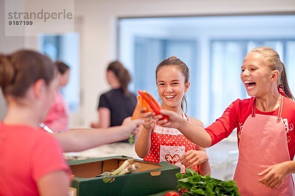 Teenagermädchen halten Chili und Karotten in der Küche hoch.