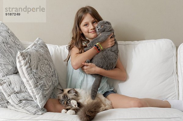 Mädchen mit zwei Katzen auf dem Wohnzimmersofa