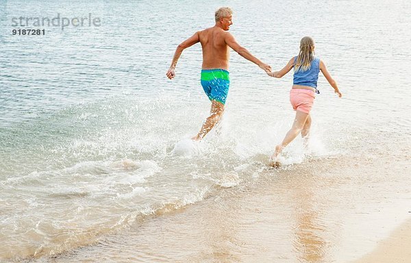 Vater und Tochter rennen und Händchen halten am Strand