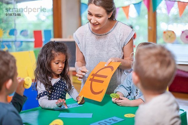 Lehrer und Schüler beim Zählen der Euro-Währung im Kindergarten