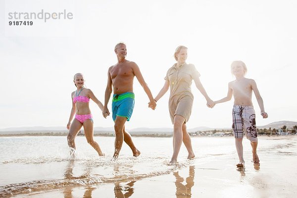 Familie mit zwei Kindern beim Bummeln und Händchenhalten am Strand