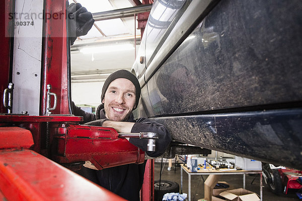 Porträt eines selbstbewussten Kfz-Mechanikers  der sich in der Werkstatt auf das Hebezeug stützt.
