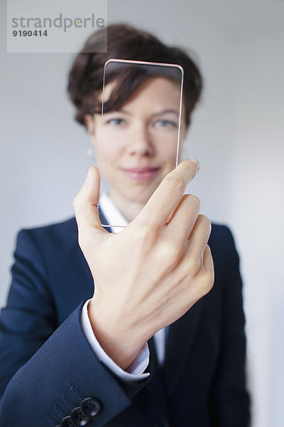 Zuverlässige Geschäftsfrau blickt durch futuristische transparente Smartphone