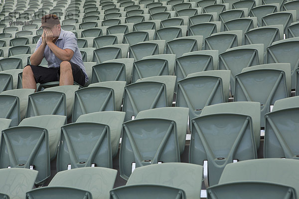 Trauriger Mann sitzt allein im leeren Stadion.