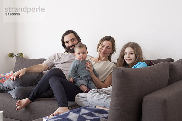 Porträt einer Familie mit zwei Kindern  die auf einem Sofa im Wohnzimmer sitzen.
