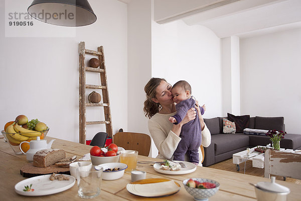 Liebende Mutter küssendes kleines Mädchen am Frühstückstisch