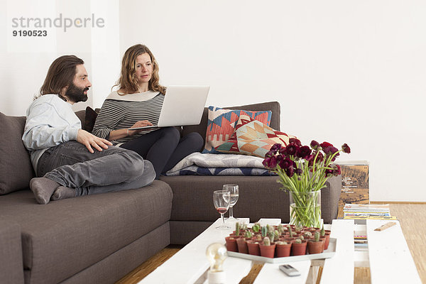 Mittleres erwachsenes Paar mit Laptop auf Sofa im Wohnzimmer
