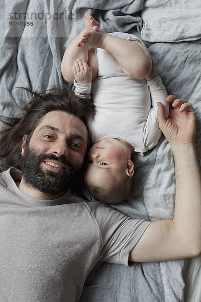 Porträt eines lächelnden Vaters mit im Bett liegendem Mädchen